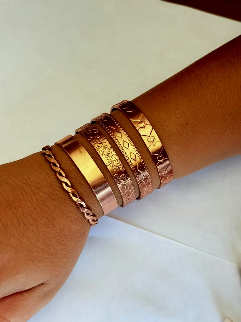 Pulso com cinco pulseiras de cobre: uma trançada, uma lisa e três com relevos de arabescos, losangos e corações